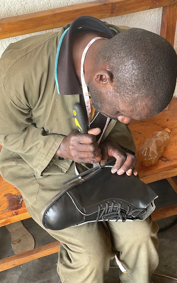 a man sits on a wooden bench and works on the sole of a black leather shoe